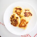 4 mashed potato cakes on a white plate sitting on a table.