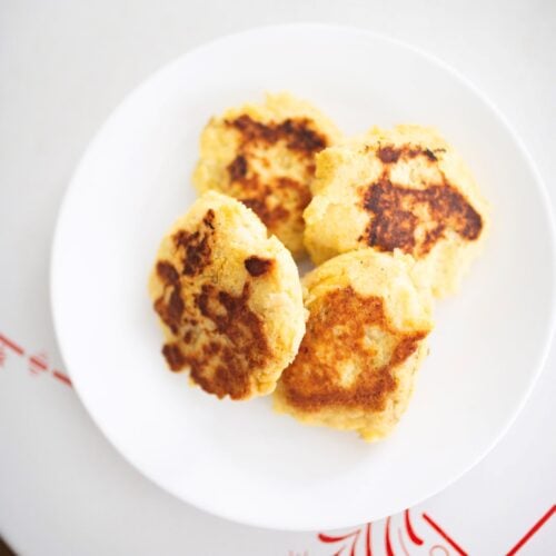 4 mashed potato cakes on a white plate sitting on a table.