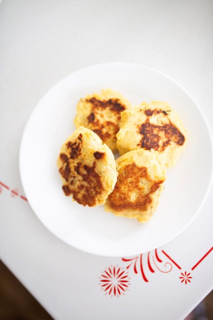4 mashed potato cakes on a white plate sitting on a table.