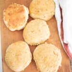 5 sourdough khorasan biscuits laid out on a wooden board with a cream and red towel beside them.