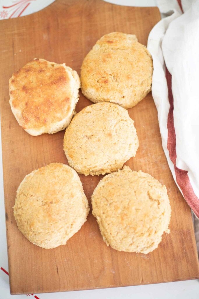 5 sourdough khorasan biscuits laid out on a wooden board with a cream and red towel beside them.