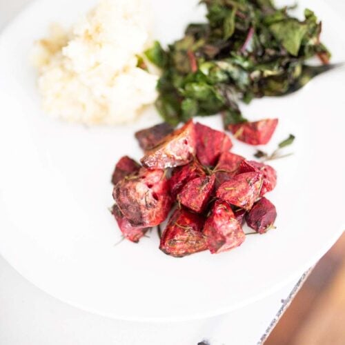 There is a white plate with rosemary roasted beets along side mashed potatoes and greens.