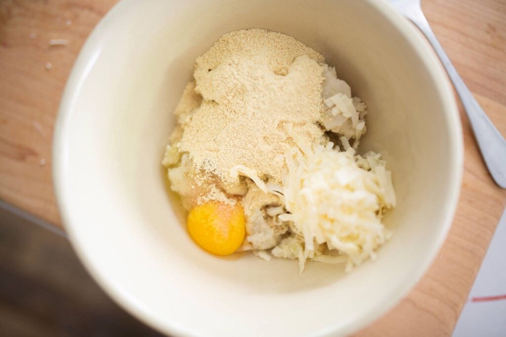 Ingredients for mashed potato cakes in a white mixing bowl.