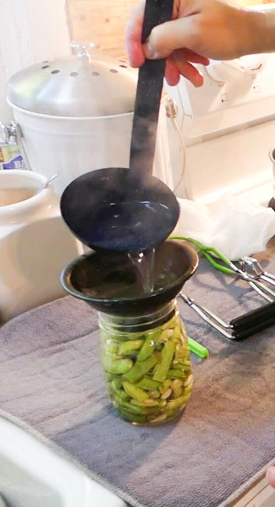A ladle is pouring boiling water into a jar of green beans.