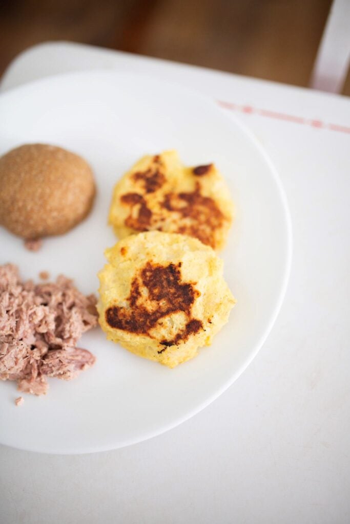 Golden brown potato cakes on a plate with some tuna and a roll.