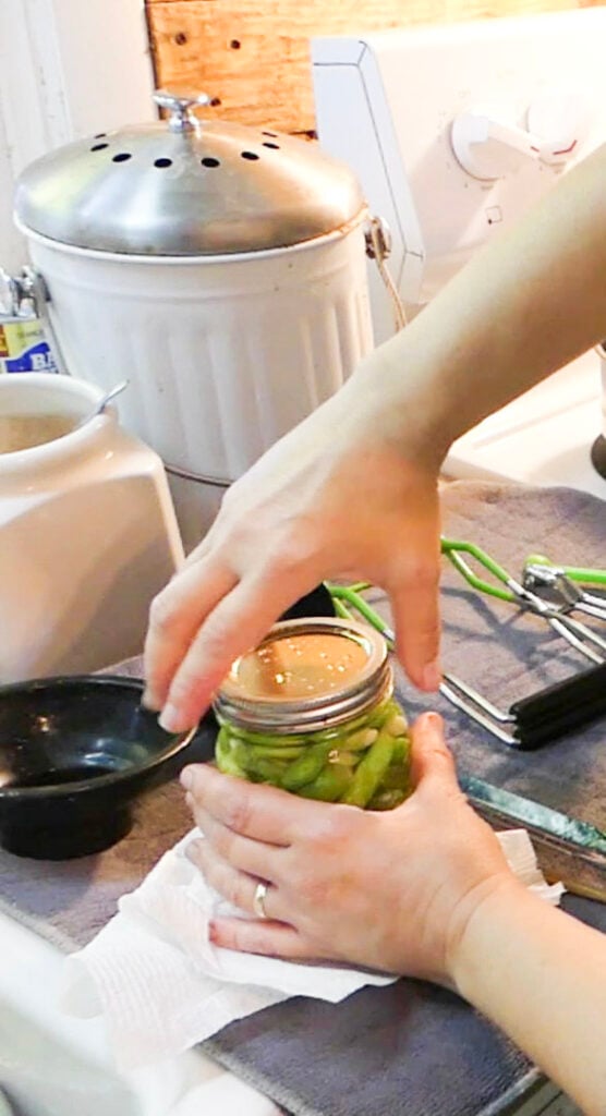 A hand is tightening a lid on a canning jar of green beans.
