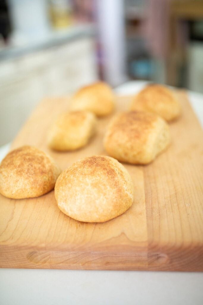 6 golden brown sourdough kamut hamburger buns on a butcher block.