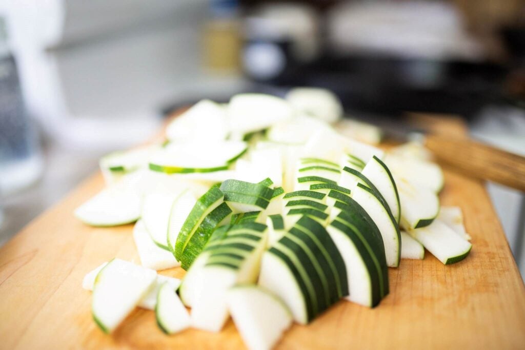 Sliced zucchini on a wooden cutting board.