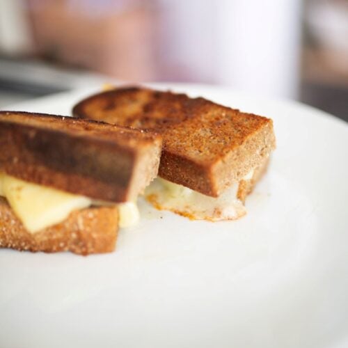 A side view of a sourdough grilled cheese on a plate cut in half.