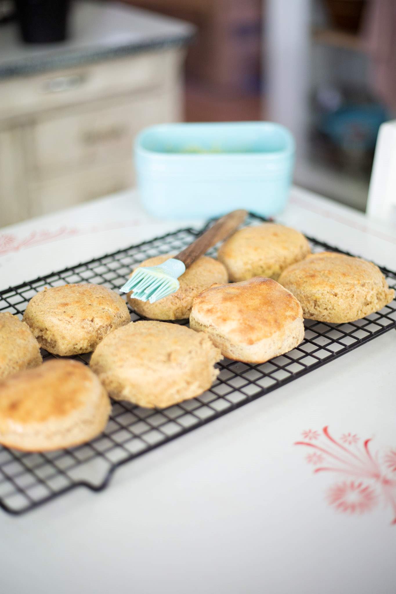 There are several sourdough khorasan biscuits on a wire cooling rack with a basting brush and teal colored butter dish in the background.