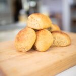 This is a side view of a stack of sourdough kamut hamburger buns on a butcher block board.