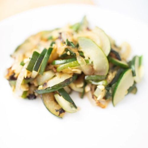 Sauteed zucchini that is golden brown on a white plate.