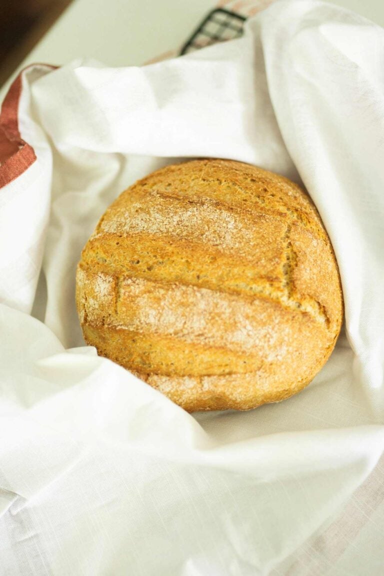 This is an artisan loaf made with fresh milled flour. It is golden brown, round, and scored with 3 straight lines across the top.