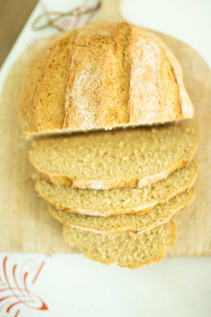 This is a loaf of fresh milled artisan bread on a wooden board with a few slices laying out in front of the loaf.