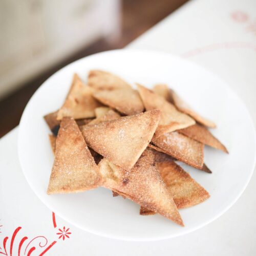 A close up of baked sourdough tortilla chips piled on a white plate