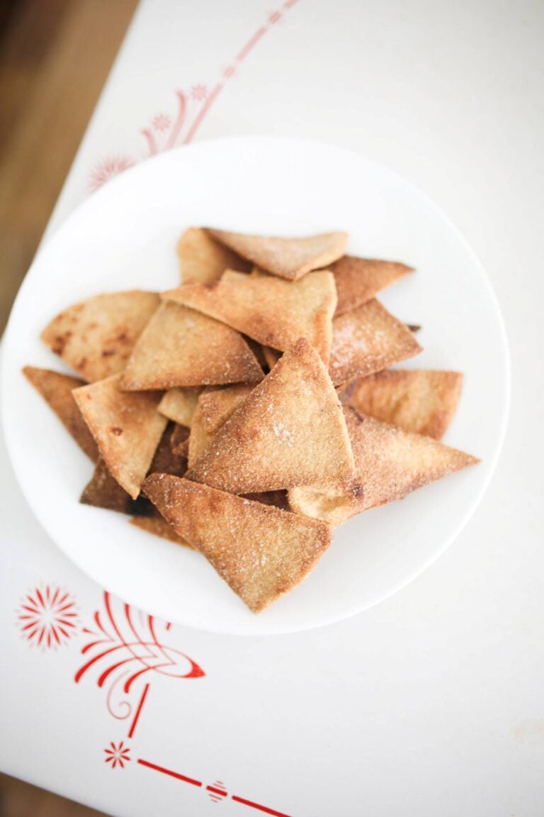 Overhead shot of baked sourdough tortilla chips stacked on a white plate