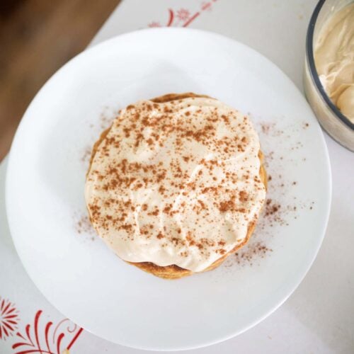 This is an overhead photo of sourdough carrot cake pancakes frosted with cream cheese frosting and dusted with cinnamon.
