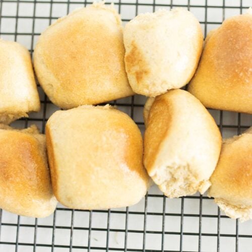 Fresh milled dinner rolls lined up on a wire rack that is black
