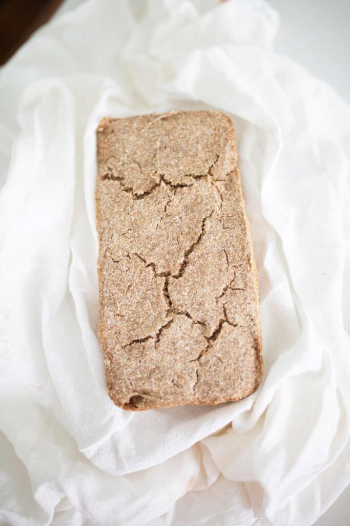 A full unsliced rye sandwich loaf nestled in a white towel.