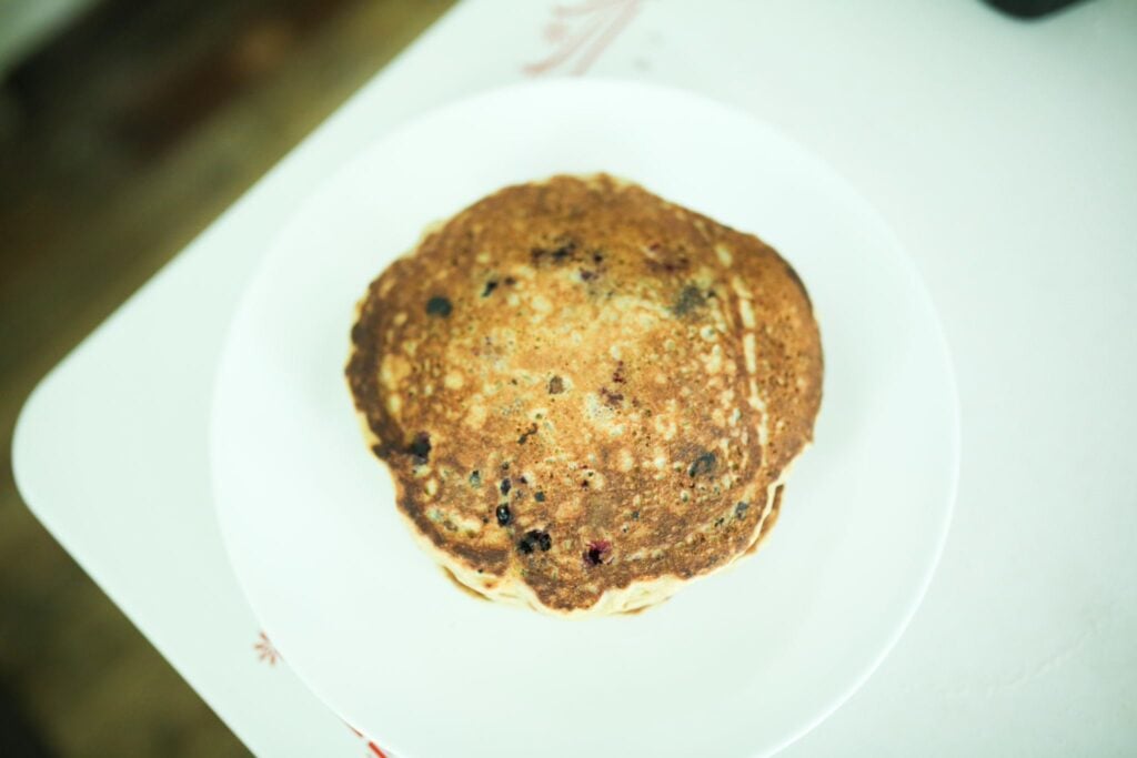 An Einkorn flour pancake on a white plate sitting on a tables edge.
