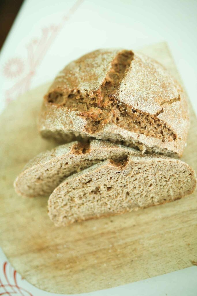 Half of a loaf of sourdough rye bread is on a cutting board with a couple of slices leaning against it to show the soft crumb.