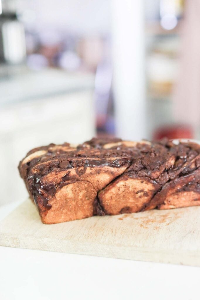 A beautiful loaf of sourdough chocolate babka on a cutting board. The loaf is golden brown and swirled with chocolate.