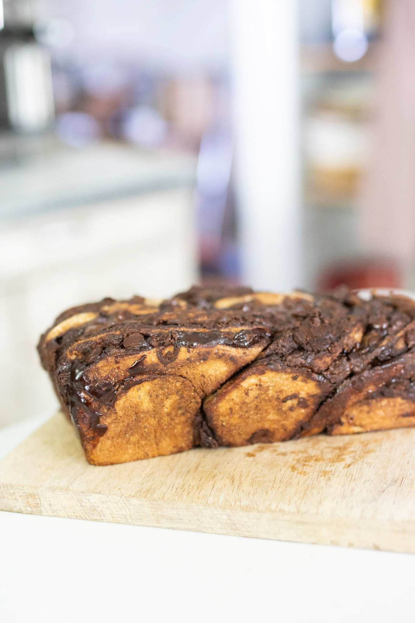 This is a loaf of sourdough chocolate babka on a wooden cutting board. It is swirled with chocolate and is golden brown.