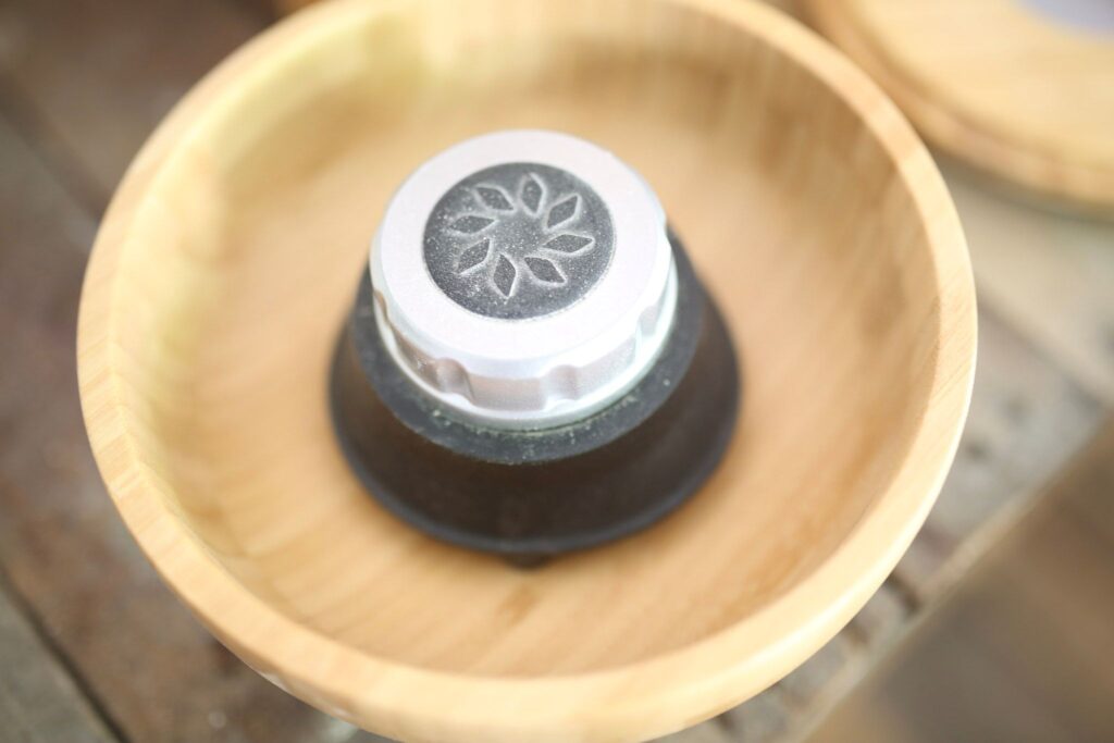 This is the hopper of the nutrmill harvest grain mill. It is wood and has a silver topped black knob for adjusting the grind.