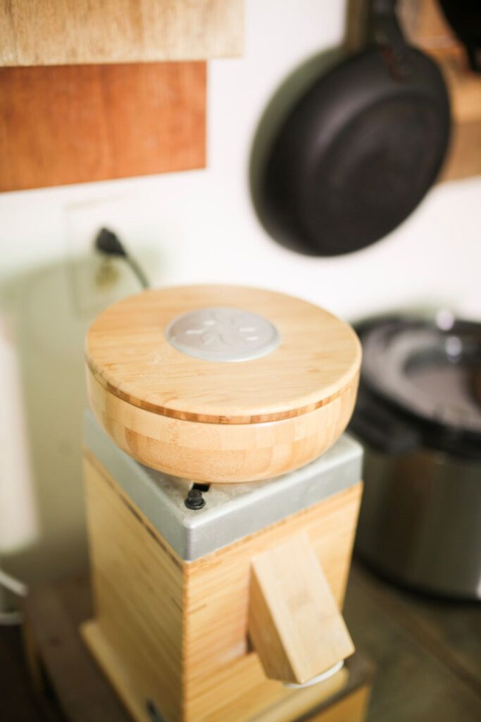 The nutrimill harvest grain mill from above to see the lid which is wooden with a silver disc in the center.
