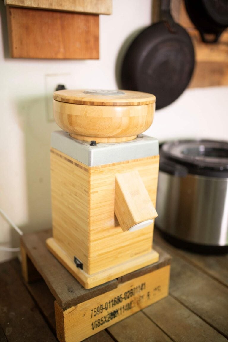 The nutrimill grain mill on a wooden stand. It is light wood with a silver trim piece.