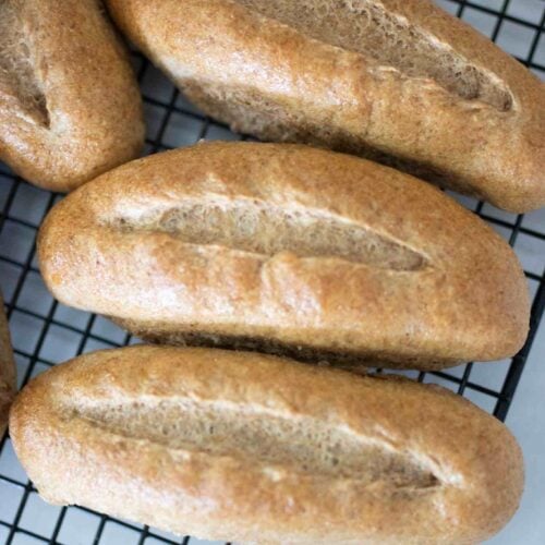 3 fresh milled hoagie rolls on a wire rack.