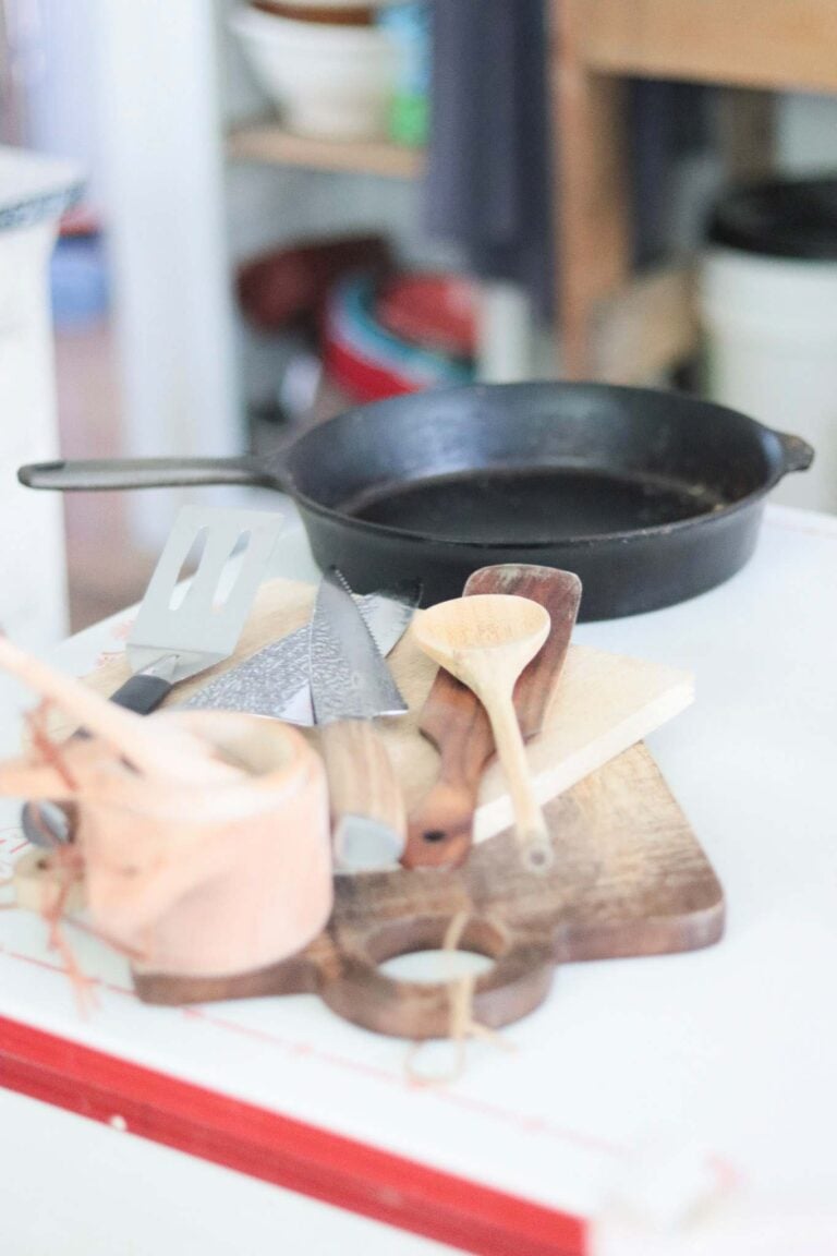 Kitchen Essential Tools laid out on a white and red table. Cast iron, wooden boards, knives, utensils.
