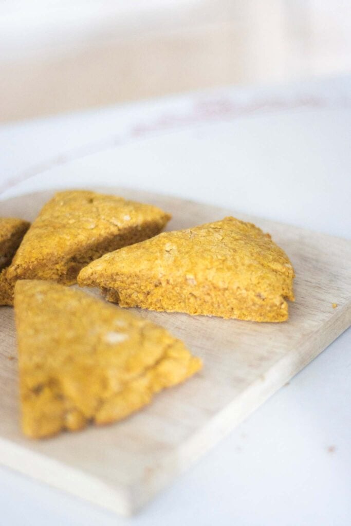3 fresh milled pumpkin scones sitting on a light wood cutting board