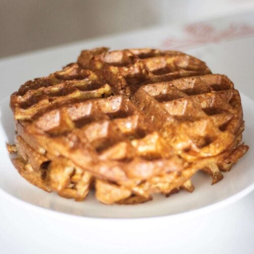 This is a close up of a stack of sourdough discard waffles on a plate on a white table top
