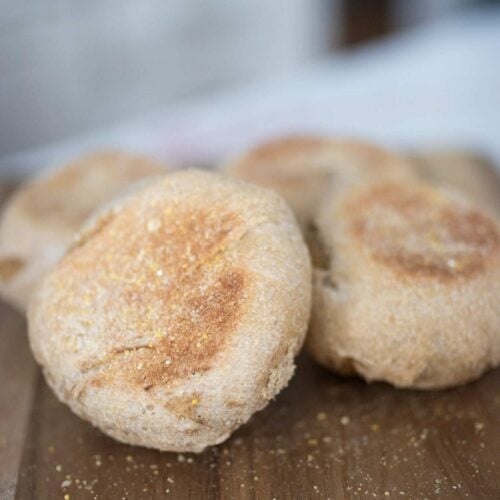 pile of sourdough english muffins on a wooden cutting board with one of them leaning on the other 3.