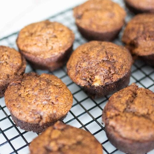 Several fresh milled gingerbread muffins on a black cooling rack.