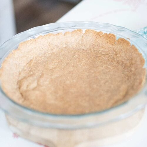 The fresh milled pie crust is par baked in a glass pie plate sitting on a wooden cutting board.