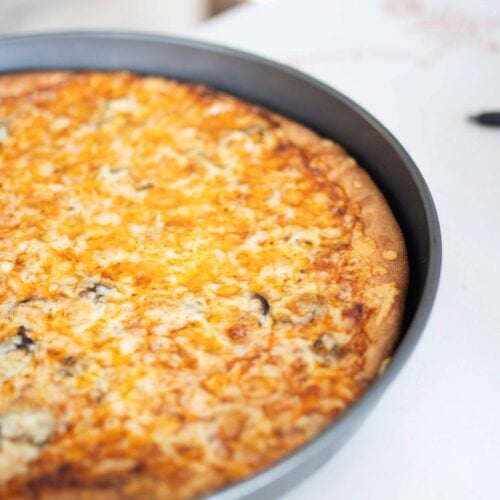 fresh milled pizza just out of the oven in a gray pizza pan. The top is golden brown.