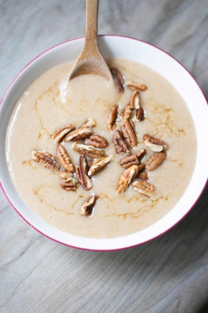 An overhead shot of cream of wheat in a red rimmed white bowl. The cream of wheat is drizzled with honey and pecans and has a wooden spoon in it.