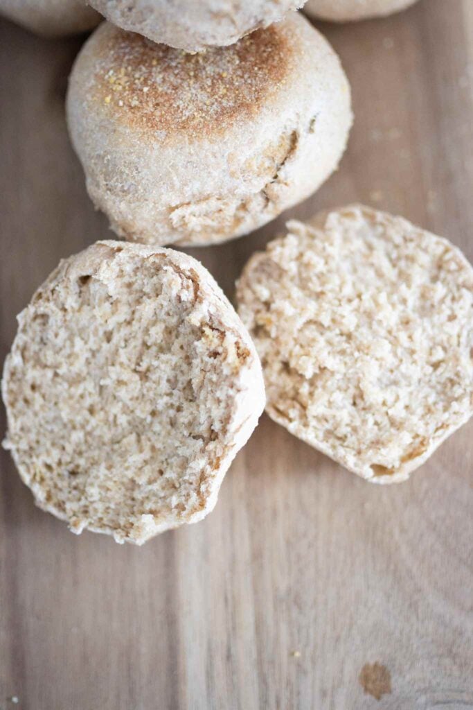 a sourdough english muffin is in half to show the airy crumb with another muffin just behind. They are on a cutting board.