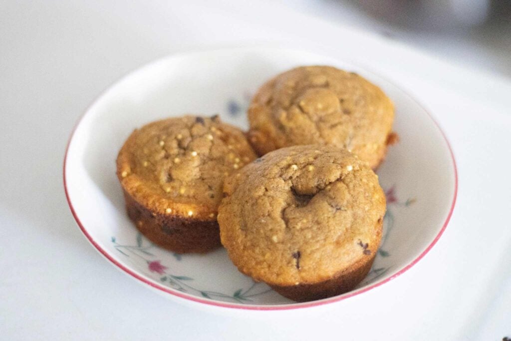 3 muffins made with ancient grains are in a white bowl with floral interior and they sit on a white counter