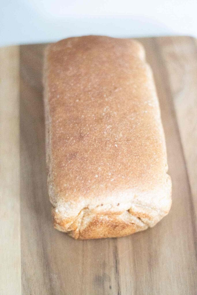 This is a full unsliced loaf of sourdough spelt sandwich bread on a cutting board.