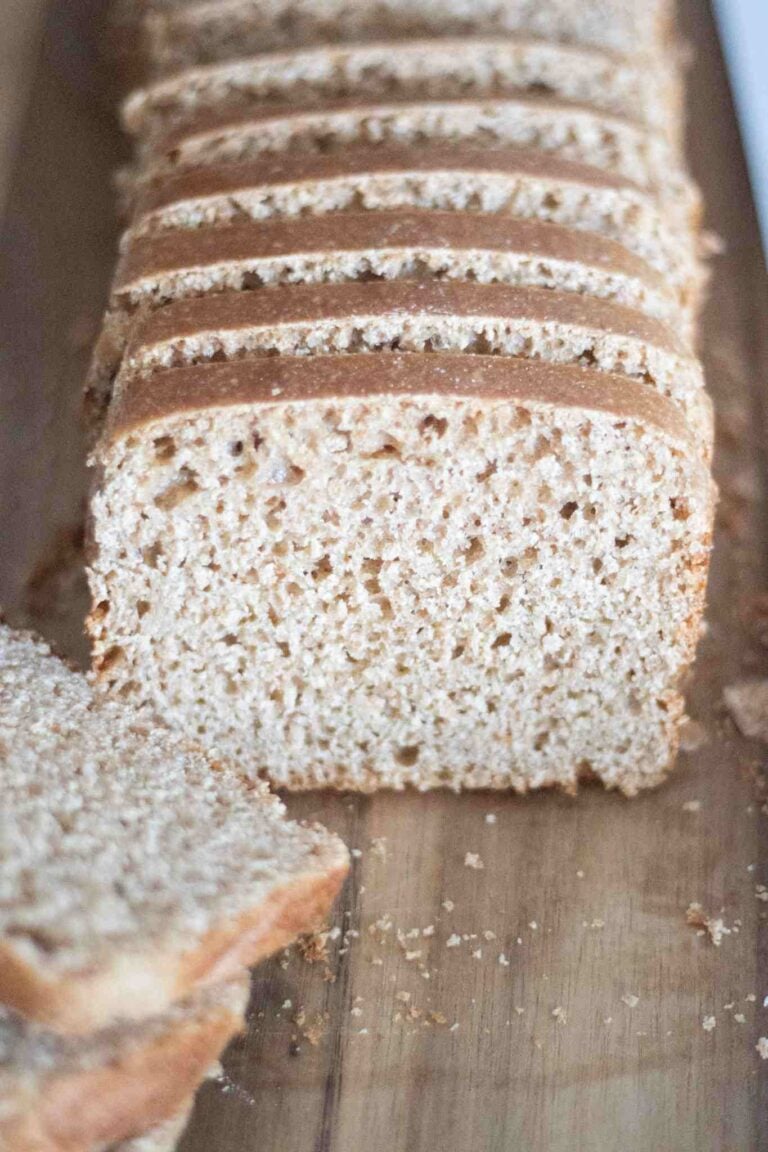 Sliced loaf of sourdough spelt sandwich bread on a dark wood cutting board. Light and airy crumb with a dark crust.