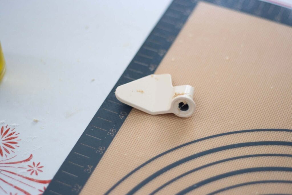 The kneading paddle of the bread machine sits on a silicone mat on the table.