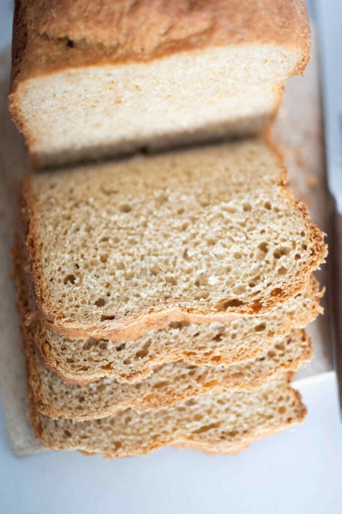 Slices of fresh milled sandwich bread made in the bread machine cascade down from the loaf sitting on a cutting board.
