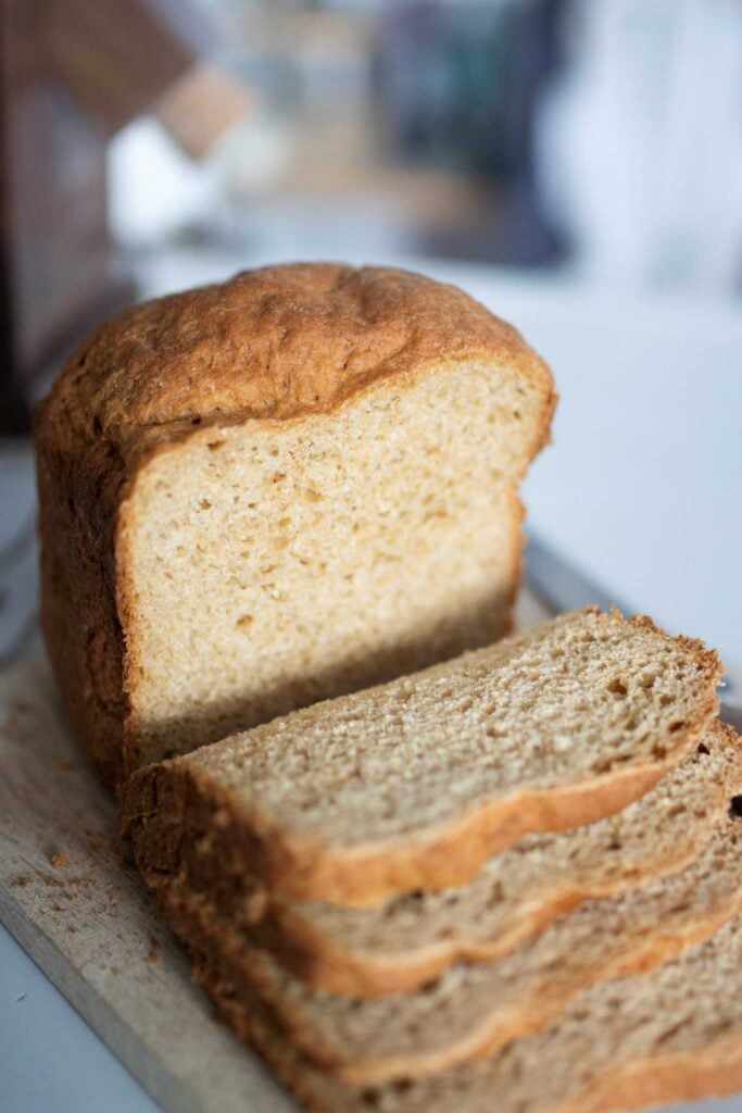 This is a side view of a sliced loaf of fresh milled sandwich bread made in the bread machine sitting on a cutting board. The loaf is half sliced.