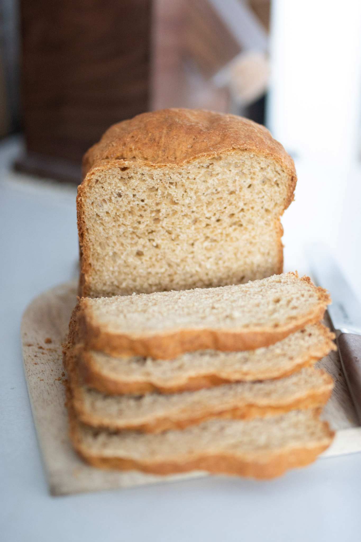 Fresh milled sandwich bread made in the bread machine sits on a cutting board and has several slices cascading down in front of the loaf.