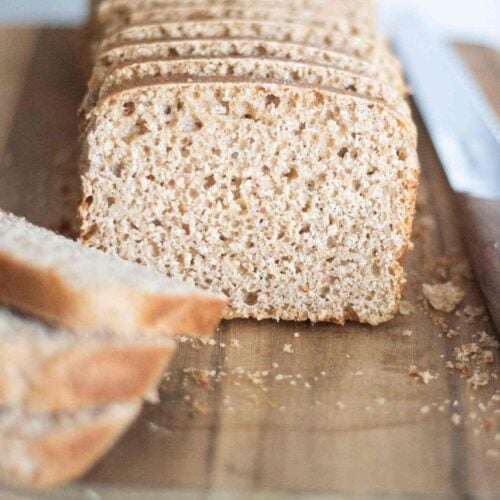 this is a sliced loaf of sourdough spelt sandwich bread on a wooden cutting board. The crumb is light and airy and the crust is golden brown