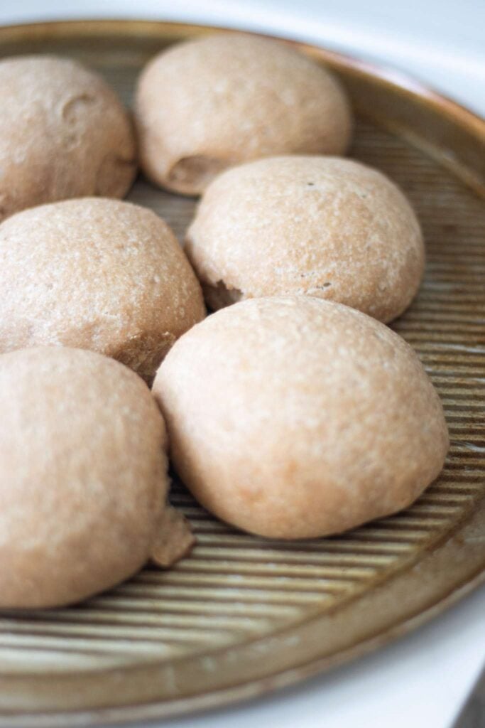 Sourdough buns that have been converted from a yeast recipe are on a metal pan.