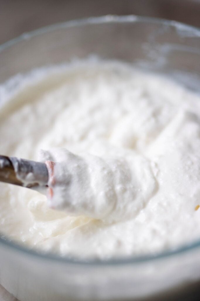 Creamy bread machine yogurt in a bowl with a spatula with a wooden handle.